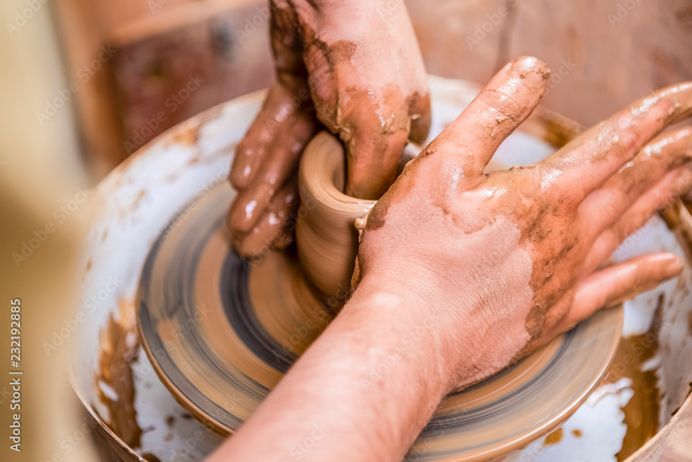 Professions and Craftmanship Concepts. Closeup of Dirty Male Hands Working with Clay on Potter's Wheel Inside of Workshop.