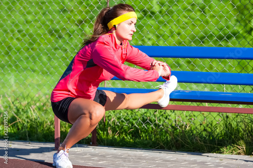 Sport Concepts. Concentrated Caucasian Sportswoman in Outdoor Sport Outfit Having Leg Muscles Stretchings With Folded Hands. Listening to Music in Headphones. photo