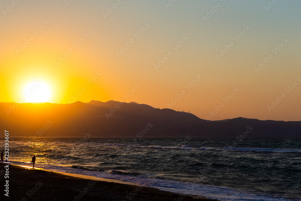 Amazing Picturesque Sunset on Heraklion Beach on Crete Island in Greece. Silhouettes Of People Wakling Along The Seashore.