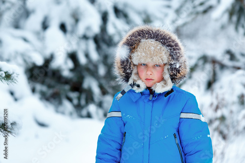 Cute little boy wearing warm clothes playing on winter forest