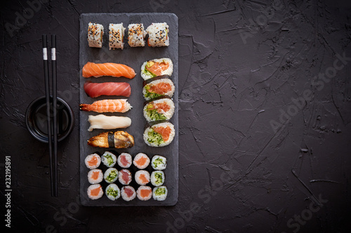 Sushi rolls set with salmon and tuna fish served on black stone board. Top view of traditional japanese cuisine. Asian food on black stone slate with chopsticks.