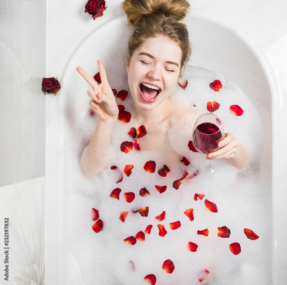 Relaxing woman smiling in hot bath with bubbles. Beautiful woman in bath with rose petals