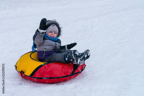 cheerful child boy in winter on a sled against a white snow