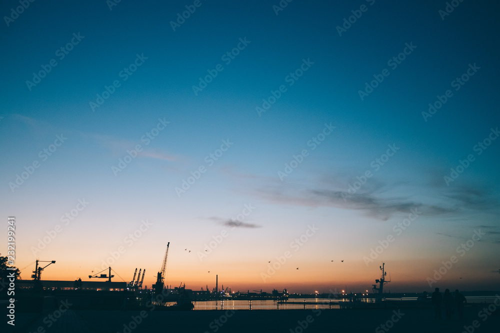 Silhouette industrial port against blue and orange sunset sky