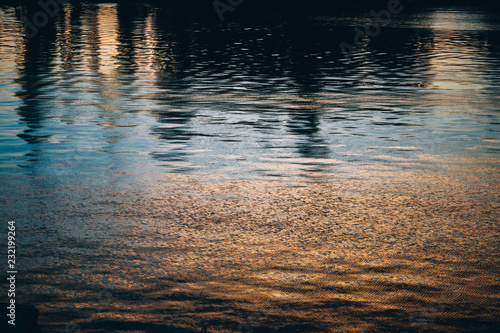 Water surface with glare of sunset sun and reflections