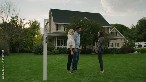 Slow motion panning shot of realtor shaking hands with couple on lawn of house for sale / Pleasant Grove, Utah, United States
