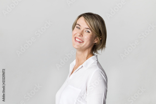 Smiling positive female with attractive look, wearing white elegant shirt posing against white wall