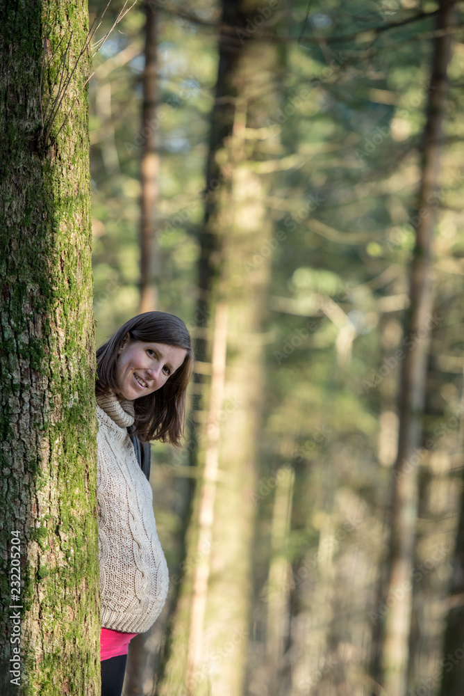 Young pregnant woman standing behind a tree in a forest Young pregnant woman standing behind a tree in a forest