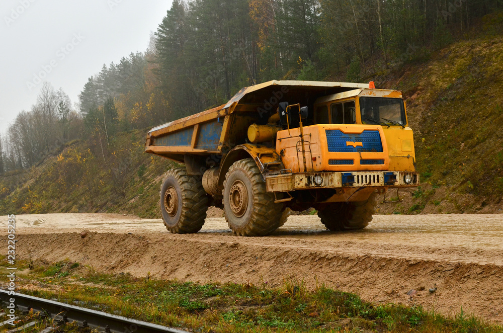 Fototapeta premium Earth mover loading dumper truck with sand in quarry. Excavator loading sand into dumper truck.Quarry for the extraction of minerals. Large quarry dump truck. Production useful minerals.