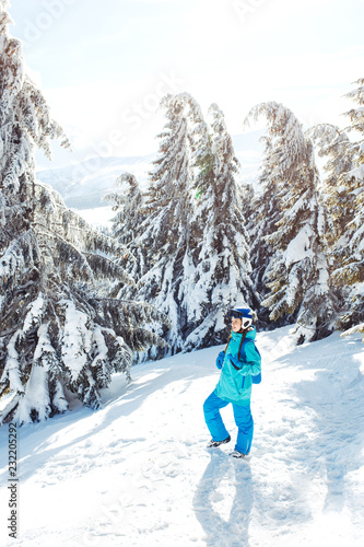 A beautiful girl in winter clothes, a blue helmet and a green jacket is having a great time in the mountains. Concept of travel, leisure, freedom, sport. Beautiful nature, places, great weather.