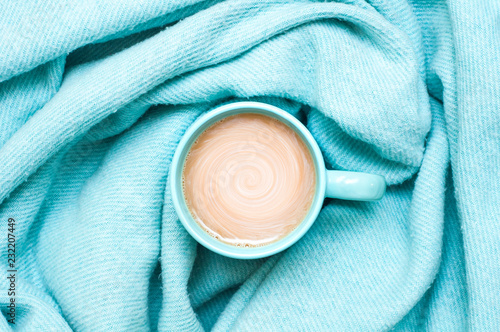 A cup of coffee with cream and a warm blanket. Turquoise colour. Top view