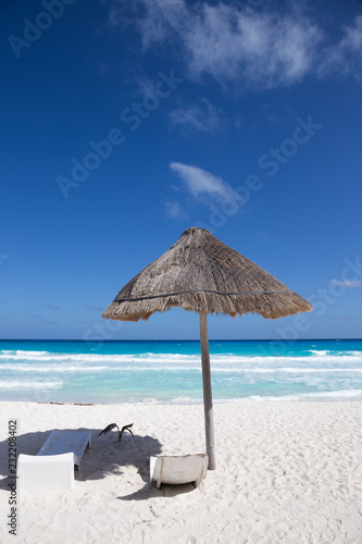 Sun umbrella with wooden lounge chairs on tropical shore
