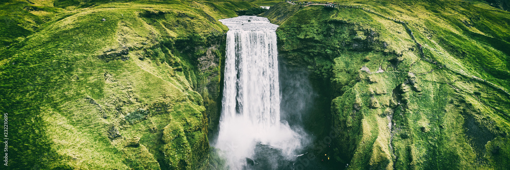 Fototapeta premium Islandia wodospad Skogafoss banner nature landscape. Panoramiczny miejsce przeznaczenia w Islandzkiej sławnej światowej punkt zwrotny atrakci turystycznej na Południowym Iceland. Widok z lotu ptaka drone góry wodospad.