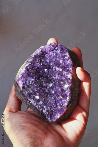 young people hand hold a selective close up focus to large cluster of shimmer shinny sparkling purple amethyst crystal gemstone reiki healing meditation on gray background low light tone with noise