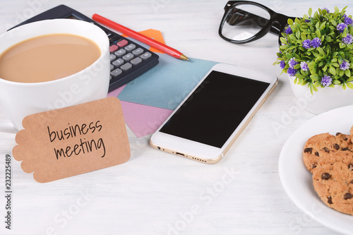 Paper card with "business meeting" text and coffee with phone, calculator, cookies and glasses