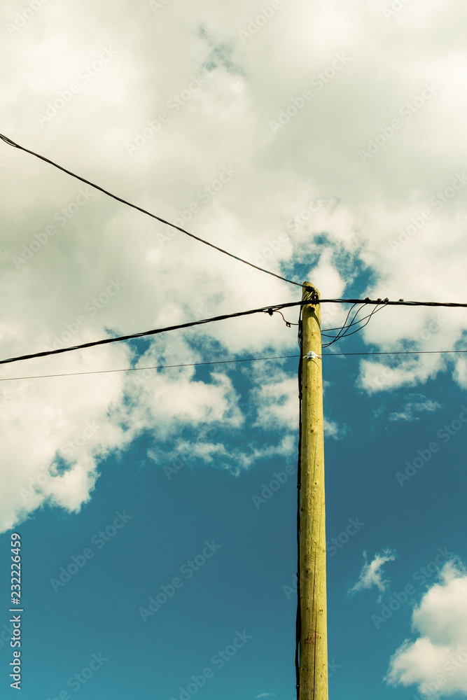 Old wooden pole and post with electrical power line against background of cloudy sky Old wooden pole and post with electrical power line against background of cloudy sky