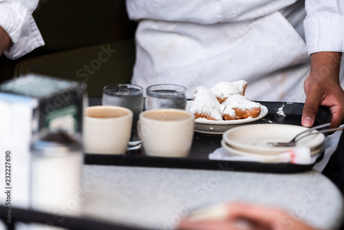 New Orleans, USA Famous cafe restaurant in Louisiana old town city with waiter placing tray at table with popular pastry beignets donut