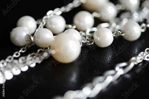 Necklace of white beads and metal chain on a dark background close up