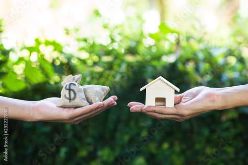 Tableau sur toile Hand holding home model change to money with green nature as background