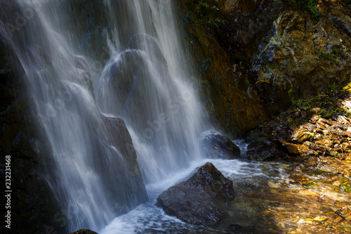 A high waterfall with white splashes of water descends from the mountain and sparkles in the sun. Attraction of Georgia Gveleti waterfall