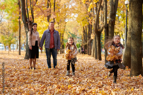 Happy family is in autumn city park. Children and parents running with leaves.. They posing, smiling, playing and having fun. Bright yellow trees.