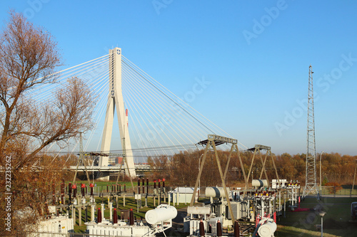  High-voltage electrical network of transformer substation on the background of a modern bridge. Industrial energy. Metal structures in the open air. Insulators and cable. Rzeszow, Poland, Europe.