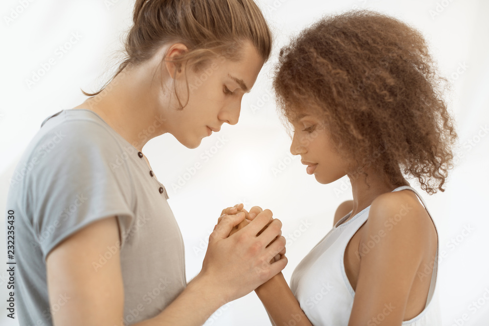 Stylish young couple holding hands and looking on each other in love. Multiethnic relationship love and people concept. Caucasian man with his afro girlfriend indoor in studio against white backgroung