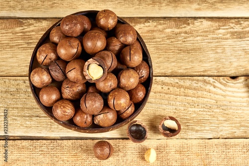 Macadamia nuts in the brown bowl on wooden table, flat lay