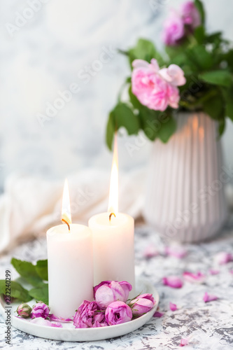 Cozy still life with candles and pink roses on a white table. Romantic home evening concept