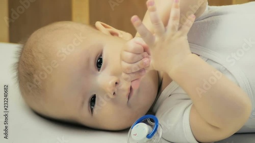 Five-month-old baby looking at the camera and sucking his finger in his bed.