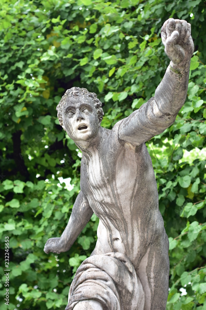 Fototapeta premium Stone statue of almost naked male in front of trees in park.