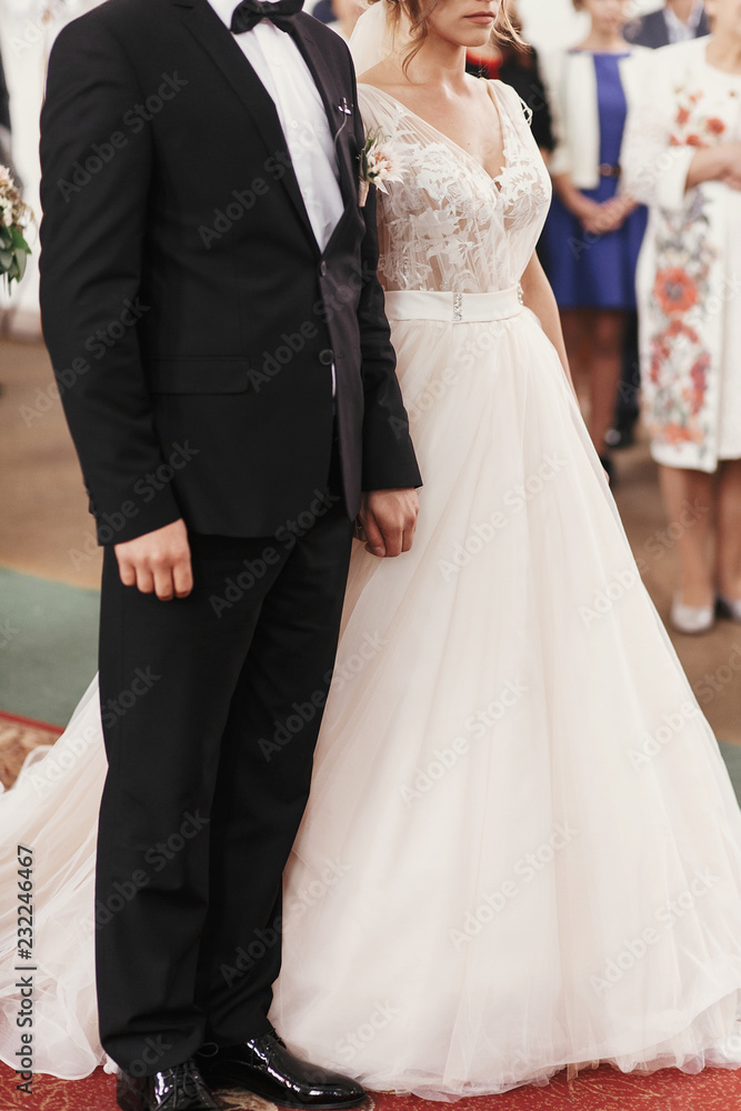 Bride and groom holding hands and standing during wedding ceremony. Spiritual couple. Wedding matrimony in church. Emotional romantic moments Bride and groom holding hands and standing during wedding ceremony. Spiritual couple. Wedding matrimony in church. Emotional romantic moments