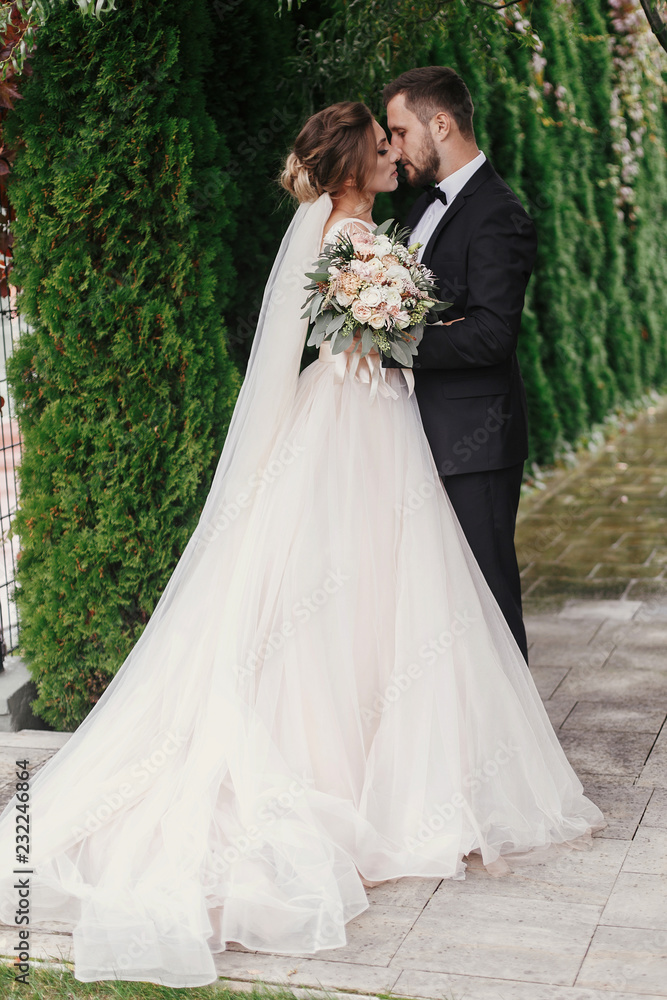 Gorgeous bride and stylish groom gently hugging on background of green trees. Sensual wedding couple embracing. Romantic moments of newlyweds. Modern wedding photo Gorgeous bride and stylish groom gently hugging on background of green trees. Sensual wedding couple embracing. Romantic moments of newlyweds. Modern wedding photo