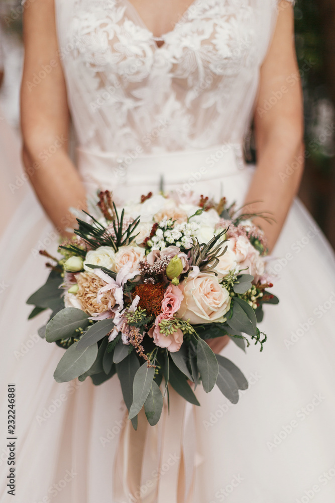 Gorgeous beautiful bride holding stylish wedding bouquet on background of modern  dress. Wedding decorations