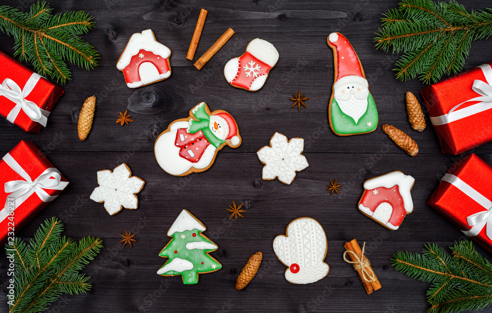 Many Christmas homemade gingerbread cookies, red gift boxes, cinnamon and fir tree branches on dark wooden background, copy space. Top view, flat lay. Santa, snowflake, mitten, house, snowman
