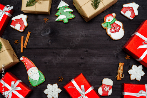 Christmas gingerbread cookies, gift boxes wrapped in craft paper with fir tree branch and red presents on dark wooden background, copy space. Top view, flat lay