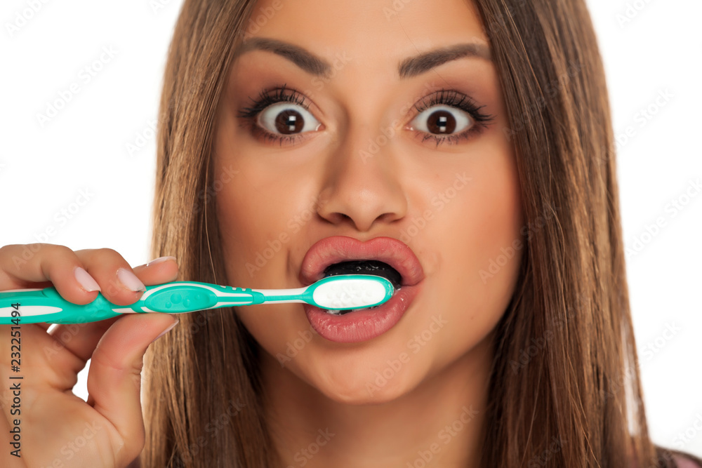 young woman brushing her teeth with black active charcoal toothpaste on white background young woman brushing her teeth with black active charcoal toothpaste on white background