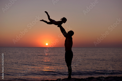 Silhouette of playing dad and daughter on the background of the sea sunset in the summer.