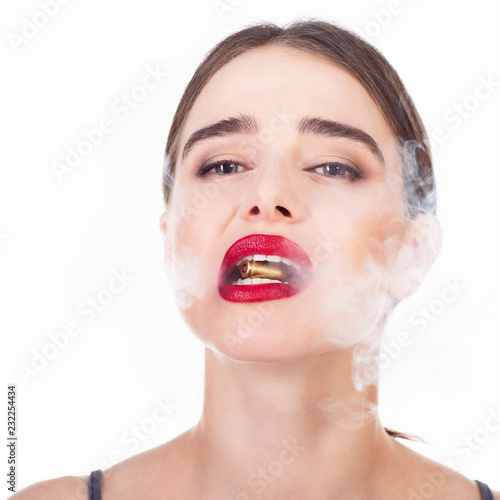 Beautiful young woman with shell in her mouth and smoke. Blue-eyed girl with red lipstick holding bullet in her teeth. Beauty will save the World, danger, war concept.