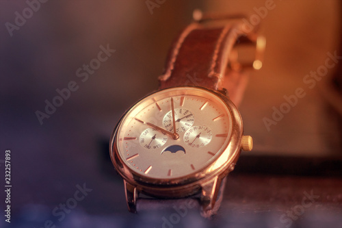 Men's gold wristwatch on a light background in the rays of the sun