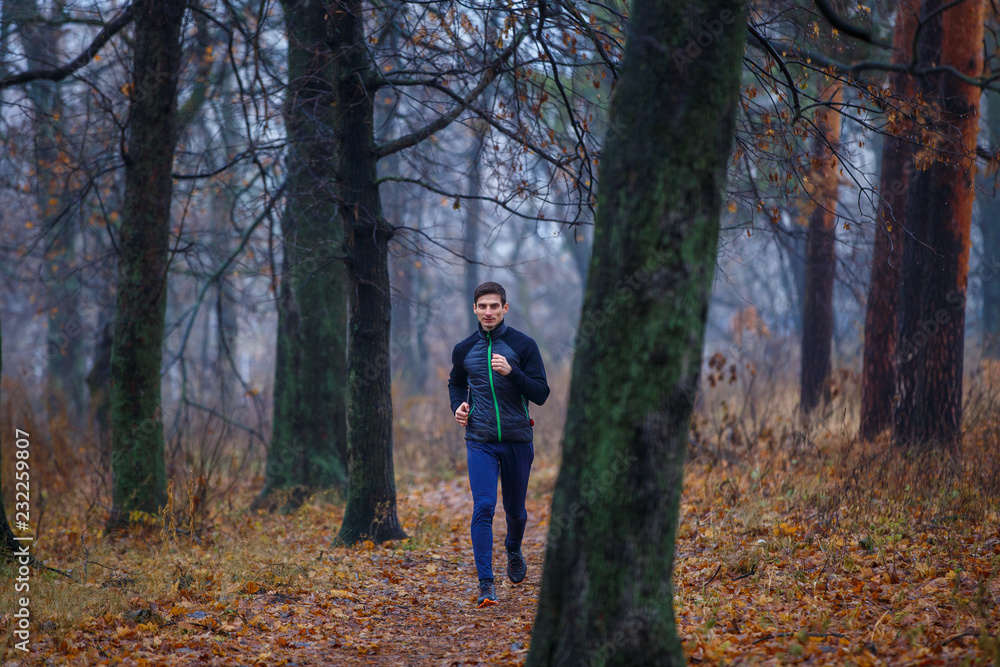 Young man jogging in autumn park in the morning