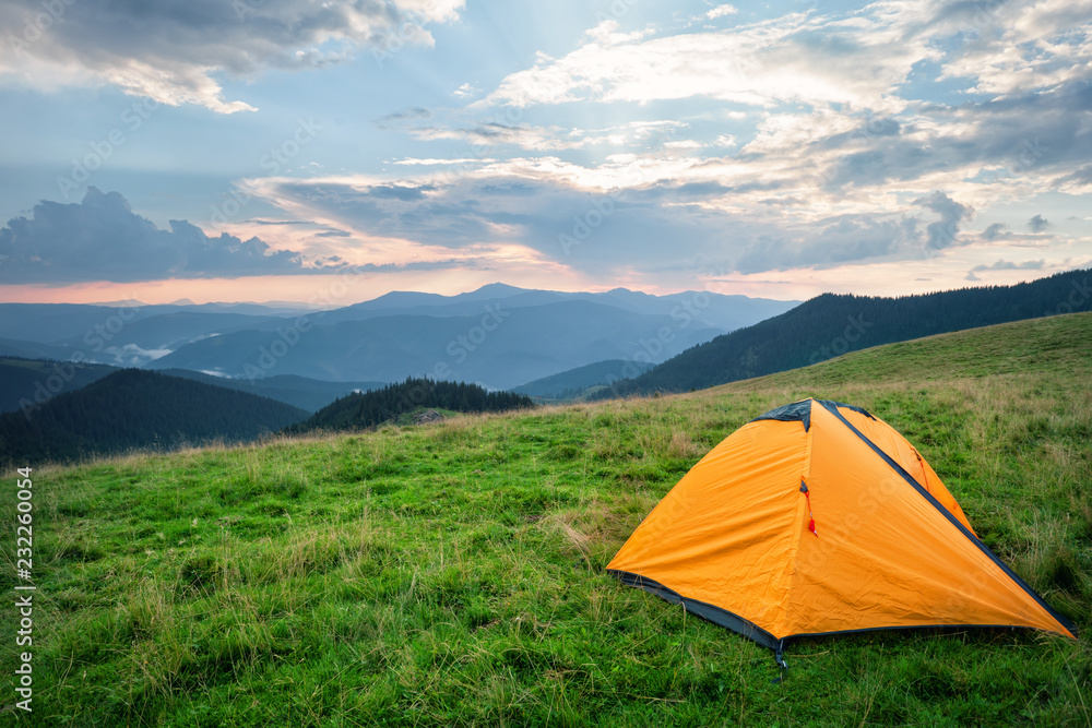 Orange tent on green grass in mountains in summer