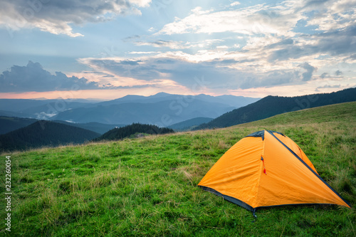 Orange tent on green grass in mountains in summer