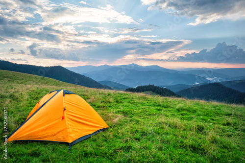 Orange tourist tent in mountains covered with green grass
