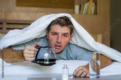 lifestyle home portrait of young exhausted and wasted man waking up suffering headache and hangover after drinking alcohol at night party lying on bed sick