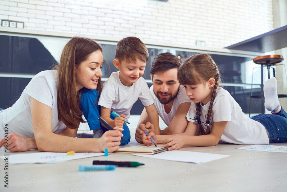 A family draws on paper lying on their free time on the floor. A family draws on paper lying on their free time on the floor.