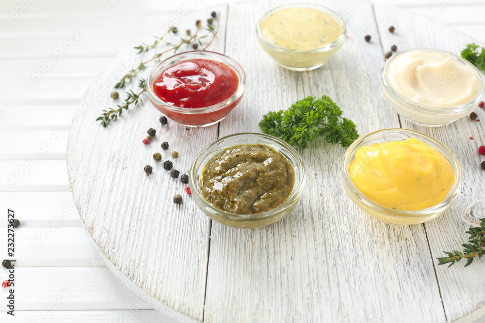 Different tasty sauces in bowls on white wooden board Different tasty sauces in bowls on white wooden board