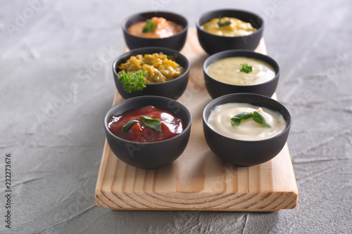 Different tasty sauces in bowls on wooden board