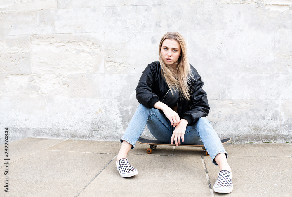Teenage girl sitting on a skate board posing for a picture Teenage girl sitting on a skate board posing for a picture