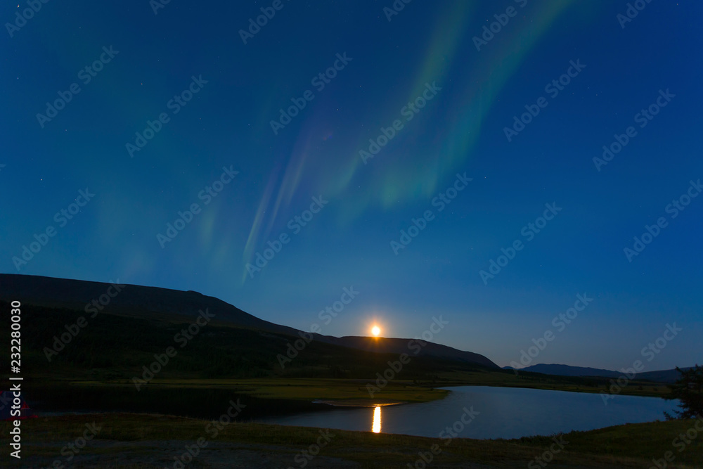 Aurora in the night sky cut the mountains, reflected in the water. Yamal. Russia